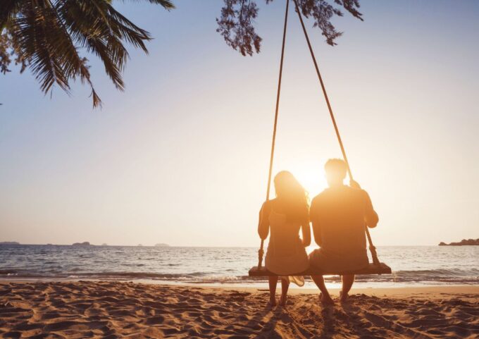 Ein Paar sitzt bei Sonnenuntergang auf einer Schaukel am Strand.