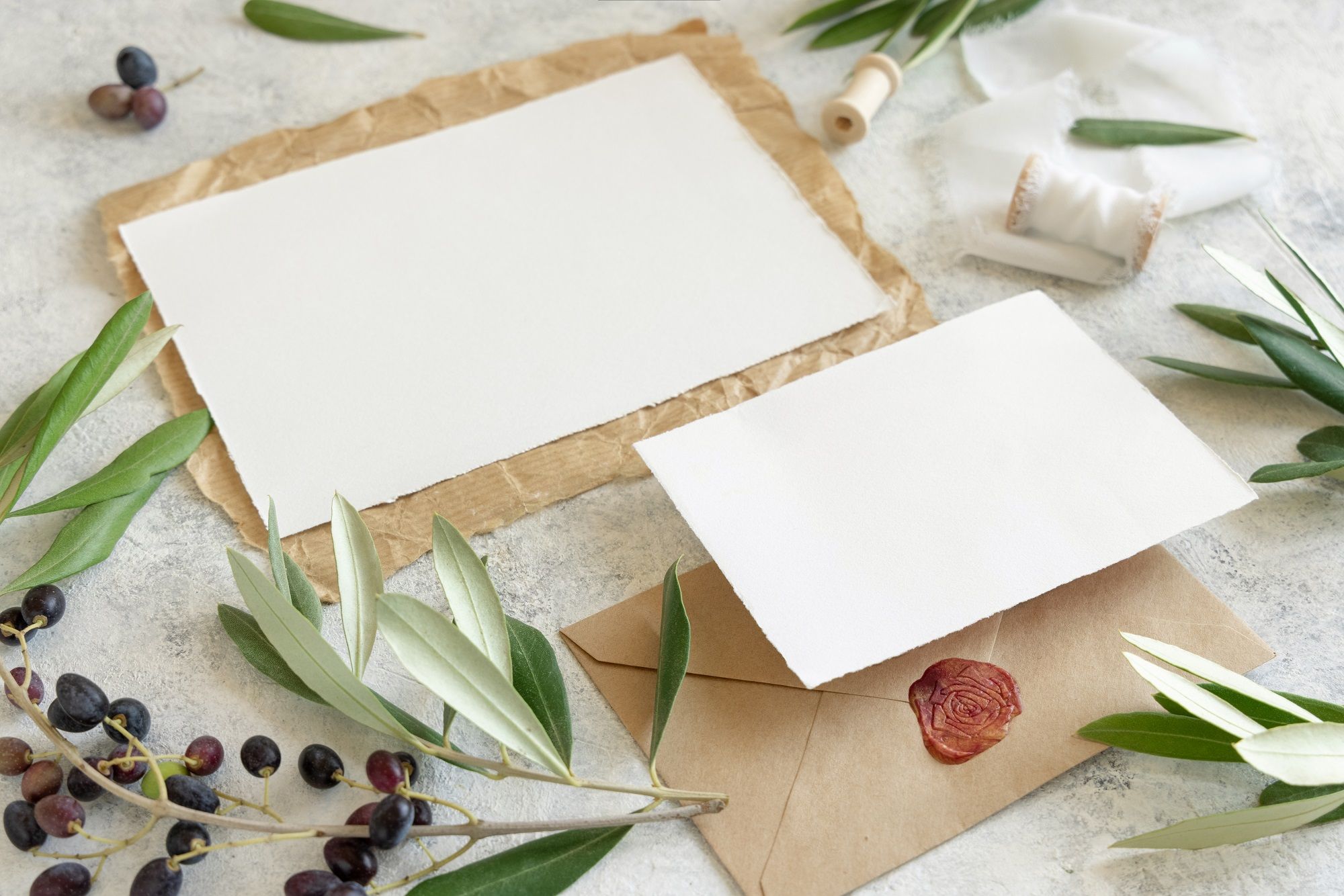 Ein weißer Umschlag mit Olivenblättern und Wachssiegel auf einem Tisch.