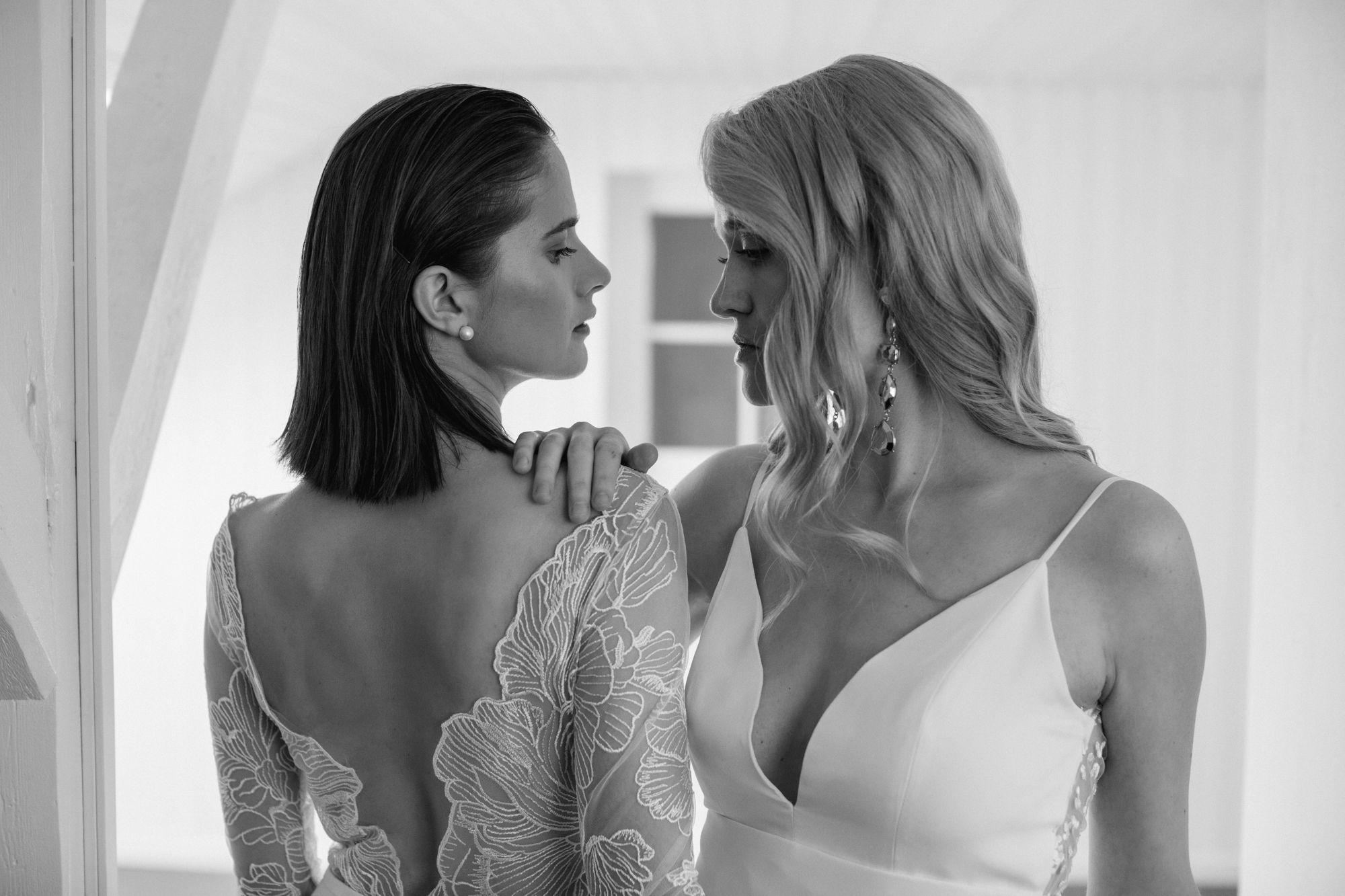 Zwei Frauen in Hochzeitskleidern schauen einander an.