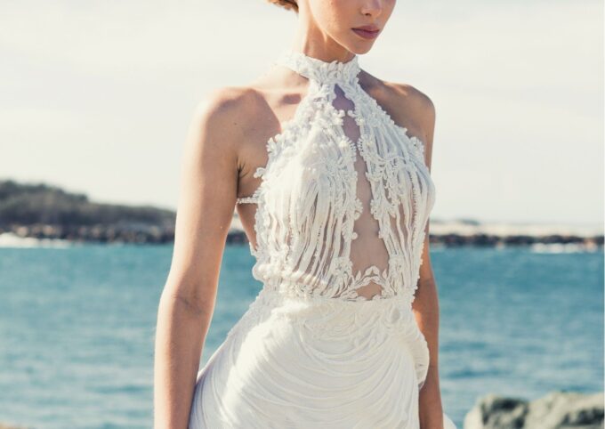 Eine Frau in einem weißen Hochzeitskleid steht am Meer.