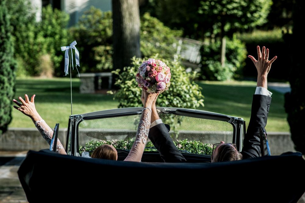 Eine Braut und ein Bräutigam in einem Oldtimer mit erhobenen Händen.