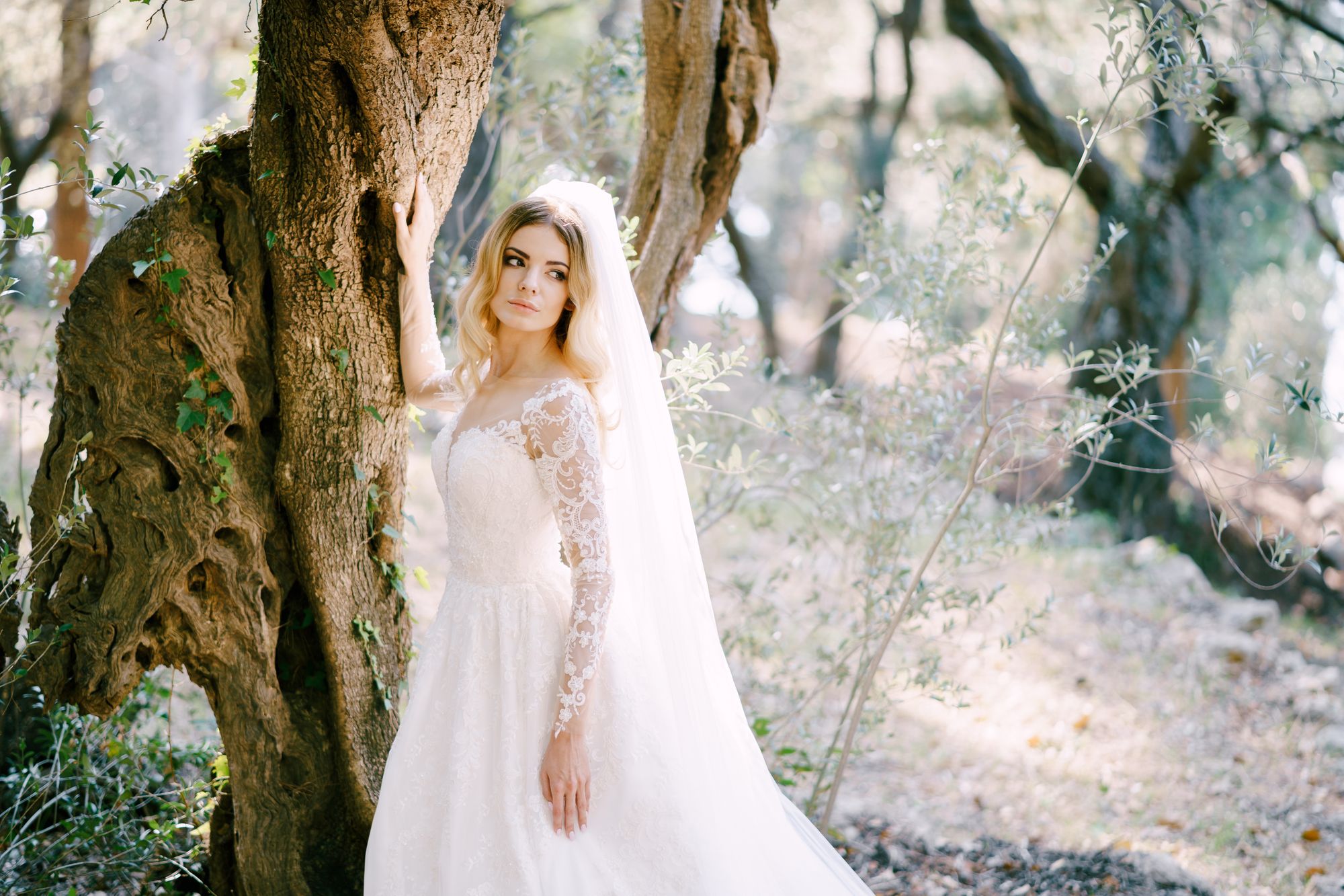Eine Braut in einem Hochzeitskleid lehnt an einem Baum.