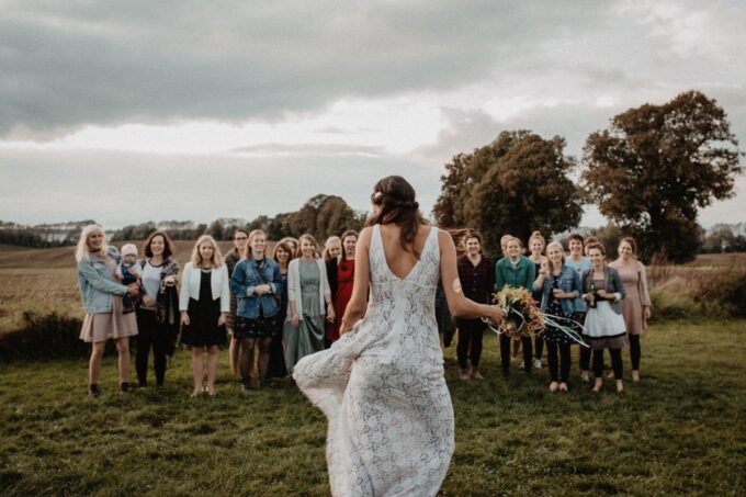 Eine Braut geht mit ihrer Hochzeitsgesellschaft auf einem Feld spazieren.