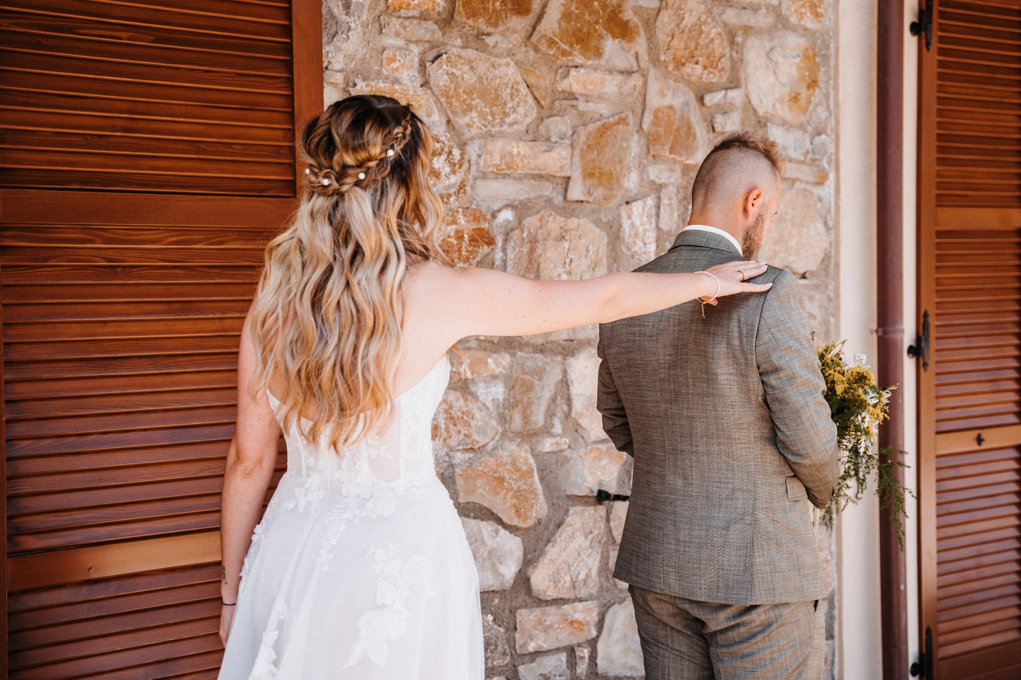 Das Brautpaar steht kurz vor dem Moment des ersten „Sehens“ am Tag der Hochzeit. Die Braut berührt Ihren Liebsten von hinten.