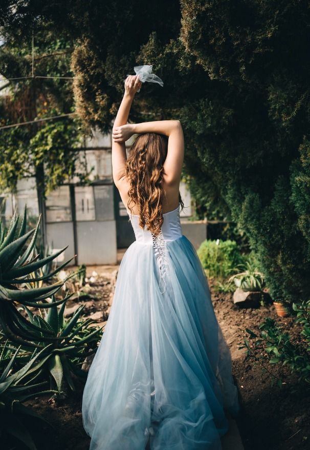 Eine Braut in einem blauen Tüllkleid steht in einem Garten.