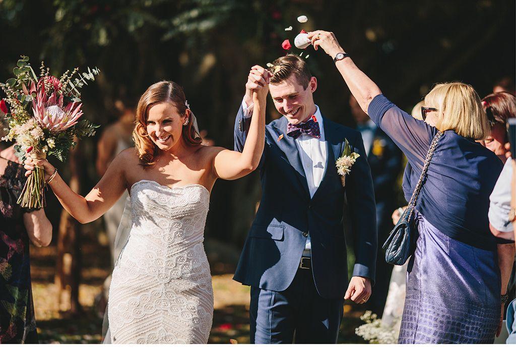 Eine Braut und ein Bräutigam gehen bei einer Hochzeit im Freien den Gang entlang.