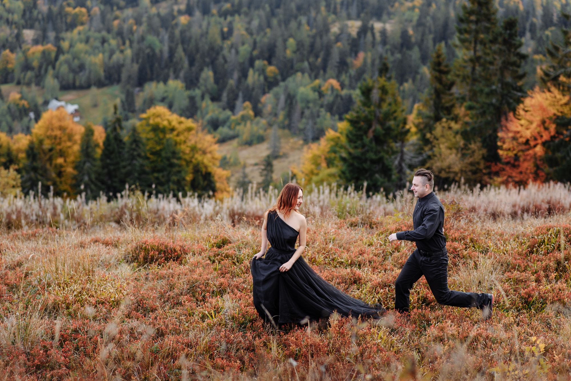 Sowohl die Braut als auch der Bräutigam sind schwarz gekleidet. Das Hochzeitspaar befindet sich mitten im Herbst auf einer Wiese und im Hintergrund ist ein Wald.