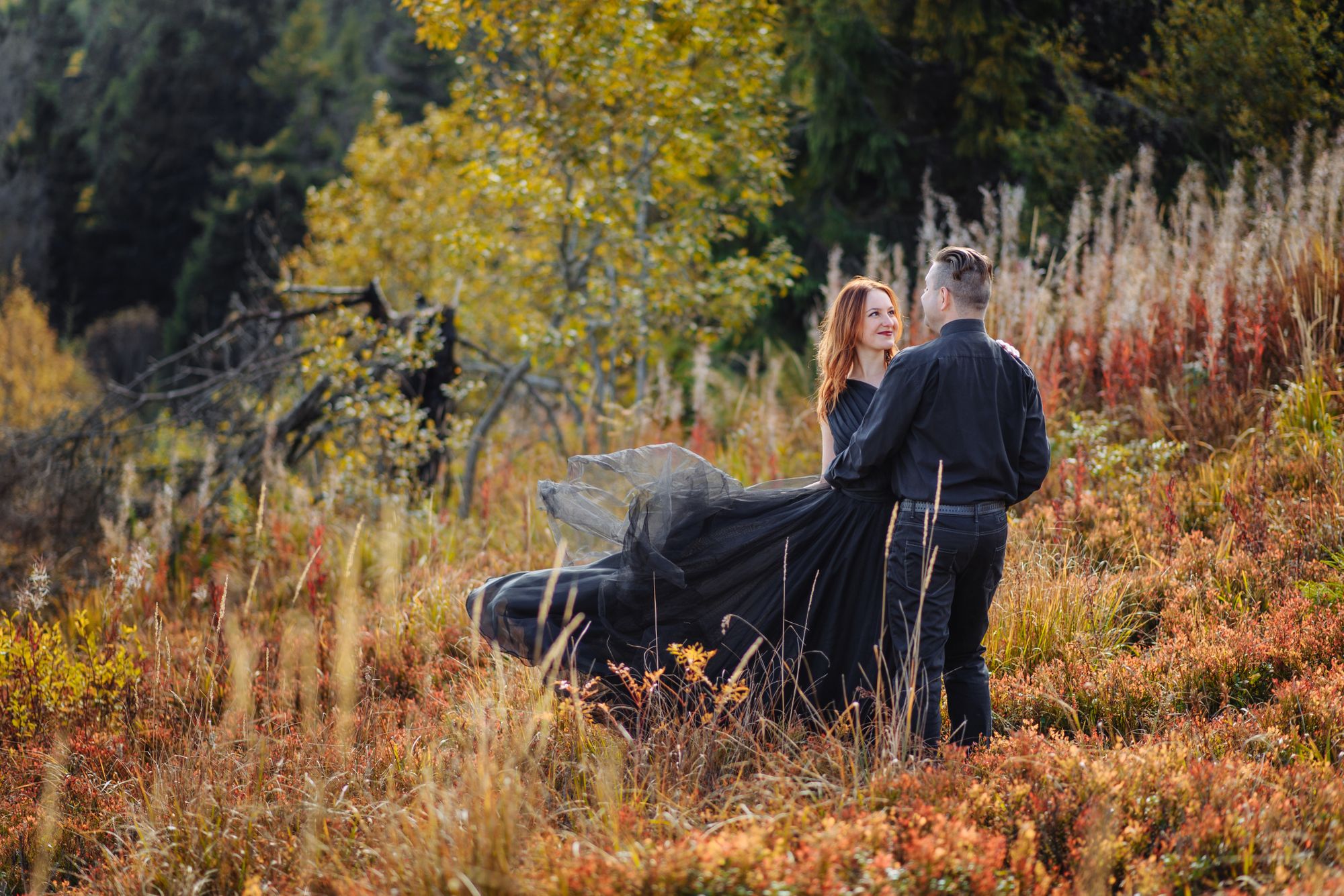 Ein Paar in einem schwarzen Kleid steht auf einem Feld mit hohem Gras.
