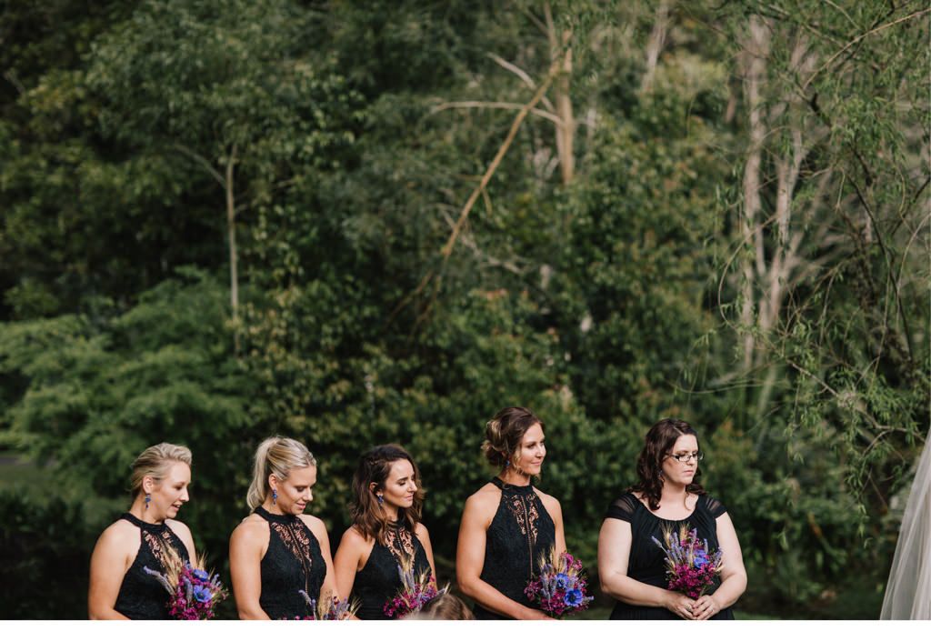 Die Brautjungfern tragen schwarze Kleider und halten bunte Blumensträuße in der Hand.