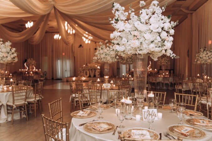 Ein Hochzeitsempfang in Weiß und Gold mit Blumen in Vasen.