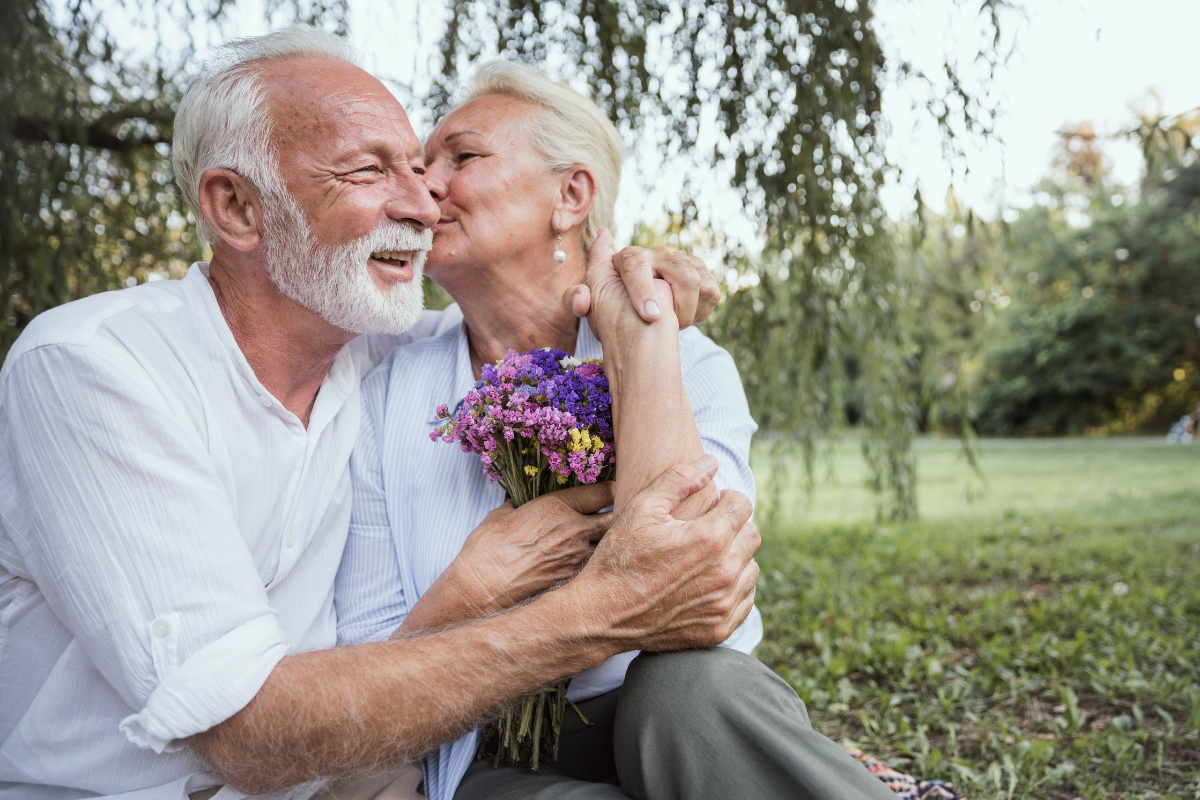 Ein älteres Paar umarmt und küsst sich in einem Park.