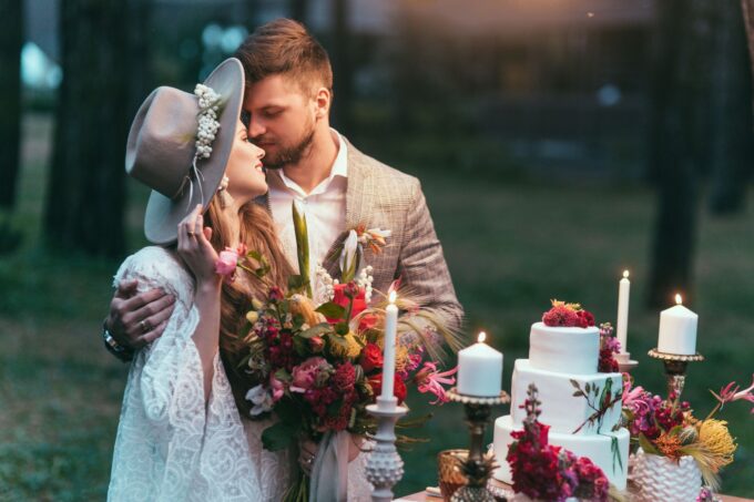 Eine Braut und ein Bräutigam küssen sich vor einer Hochzeitstorte im Wald.