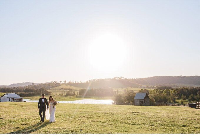 Eine Braut und ein Bräutigam gehen bei Sonnenuntergang auf einem Feld spazieren.