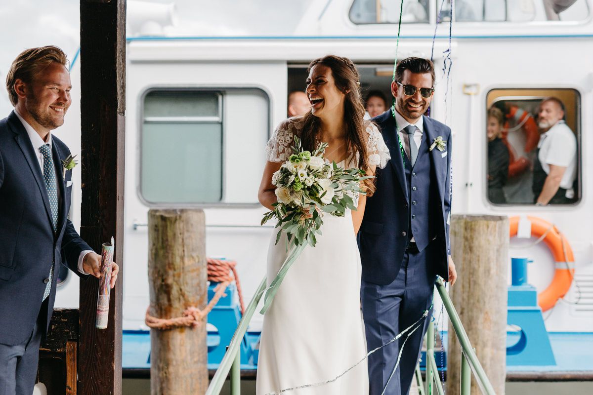 lachendes Brautpaar und Hochzeitsgast beim Schiffsanleger
