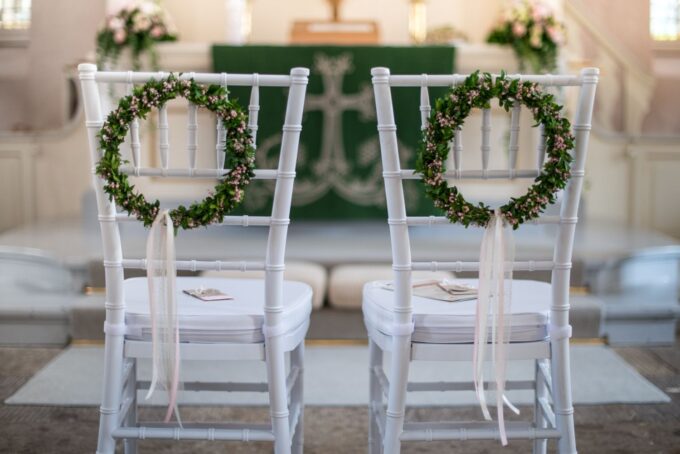 Zwei weiße Stühle mit grünen Kränzen darauf.