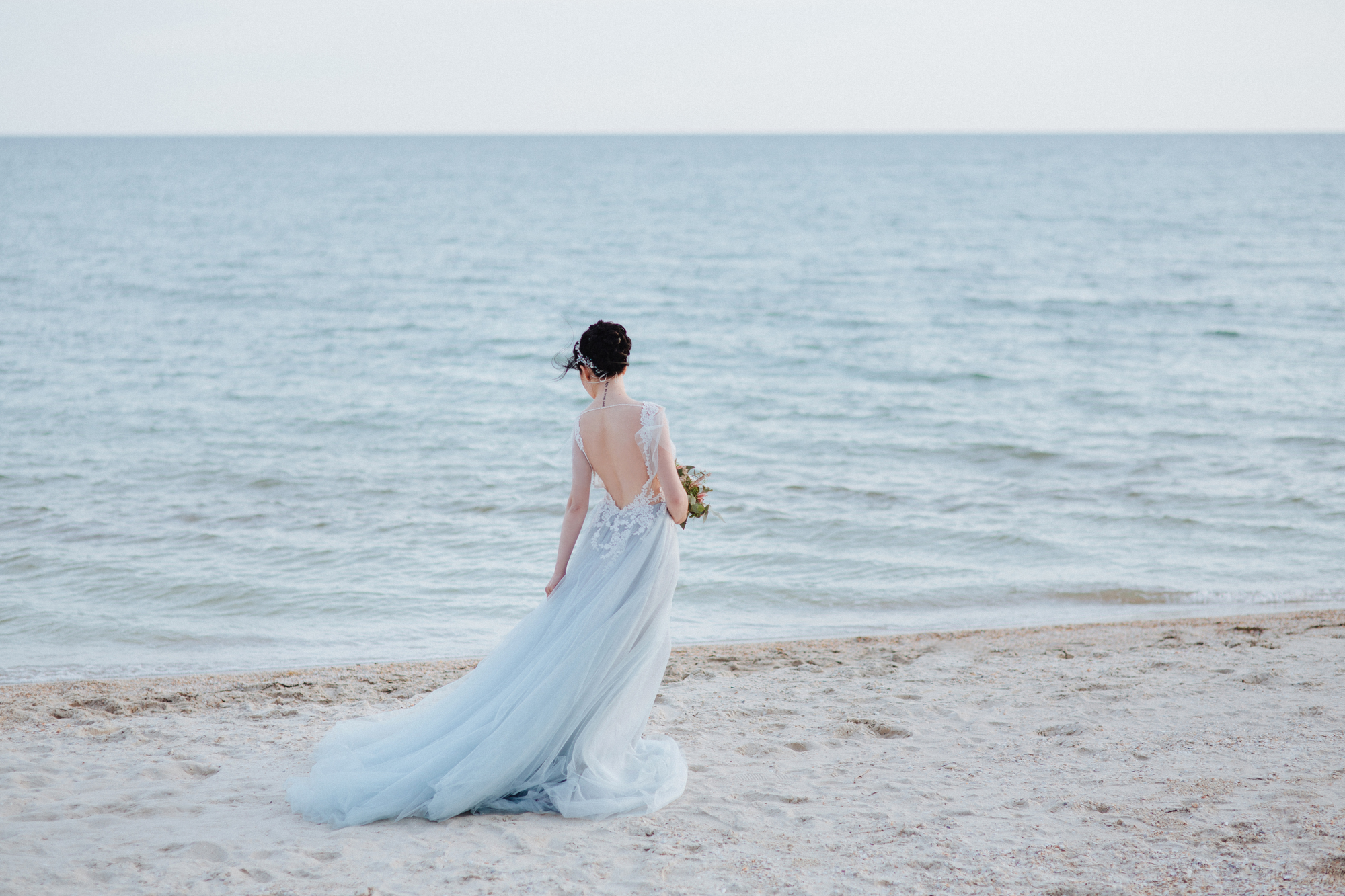 Die Braut trägt ein blaues Hochzeitskleid am Strand.