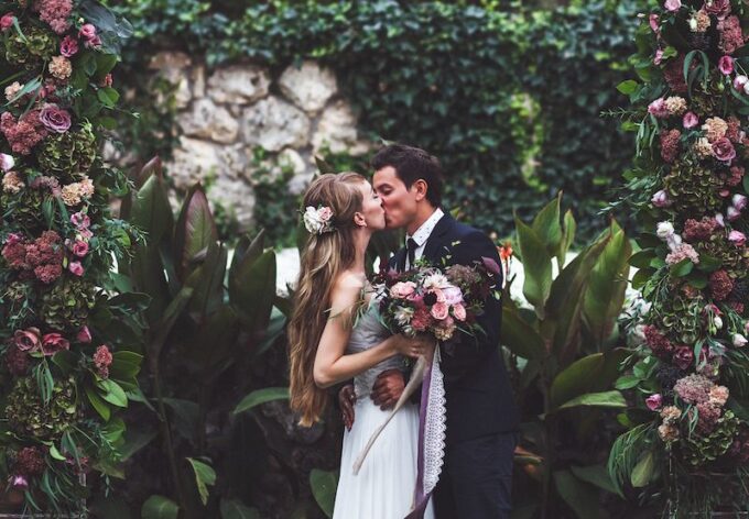 Ein Brautpaar küsst sich vor einem Blumenbogen.