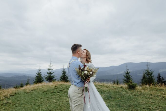 Eine Braut und ein Bräutigam küssen sich auf einem Berggipfel.