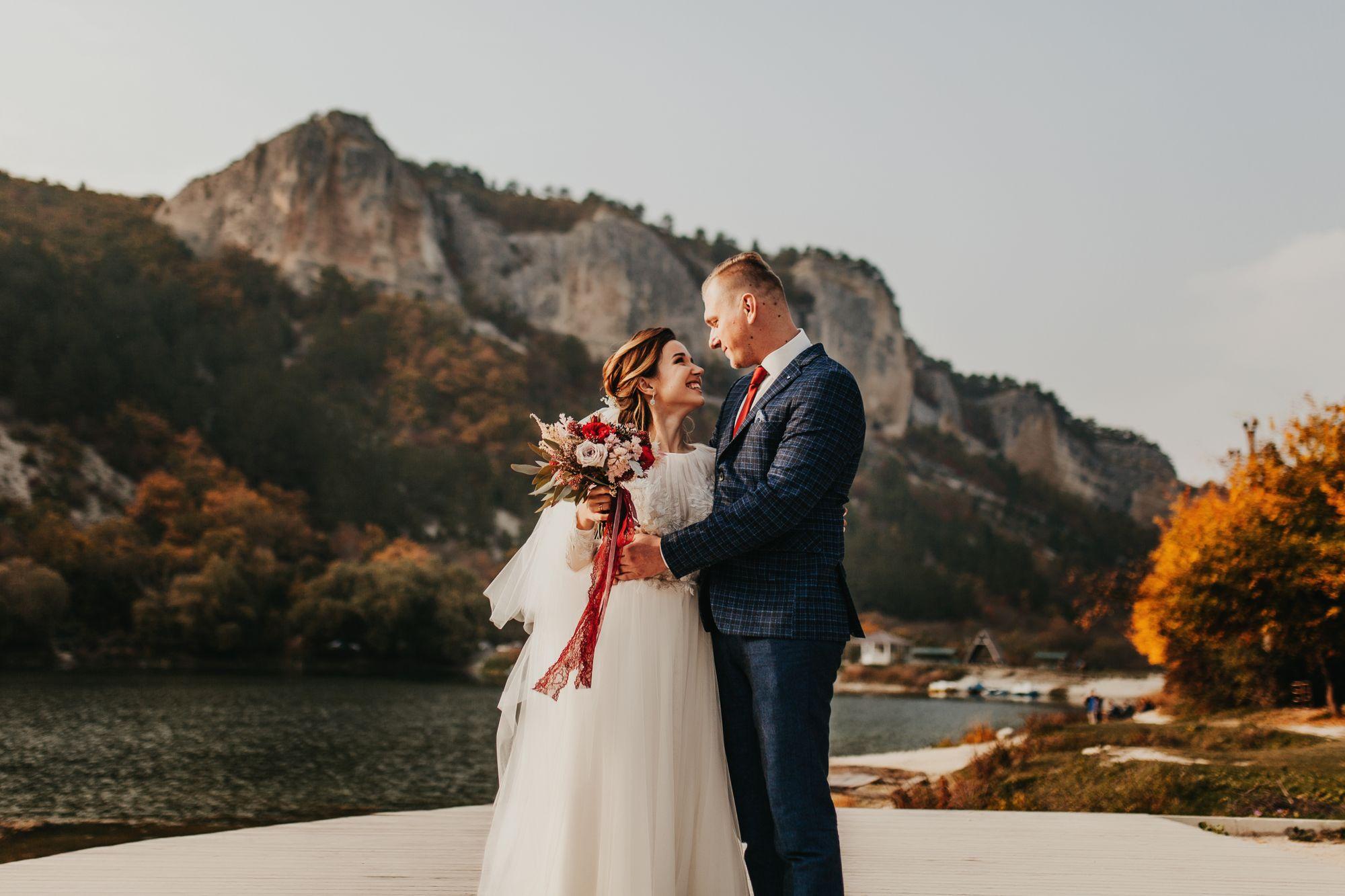 Eine Braut und ein Bräutigam stehen auf einem Steg vor einem See.