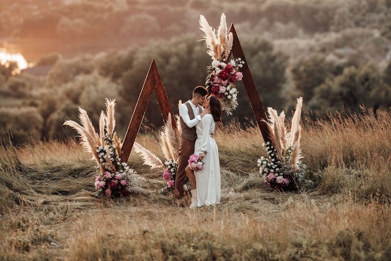 Eine Braut und ein Bräutigam küssen sich bei Sonnenuntergang auf einem Feld.