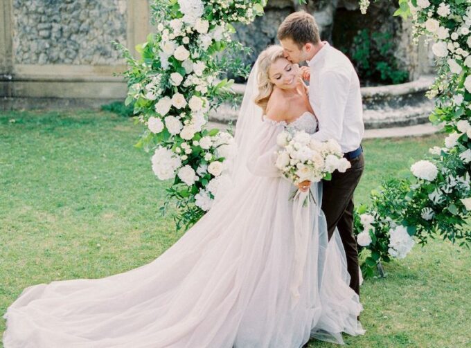 Eine Braut und ein Bräutigam küssen sich vor einem Blumenkranz.