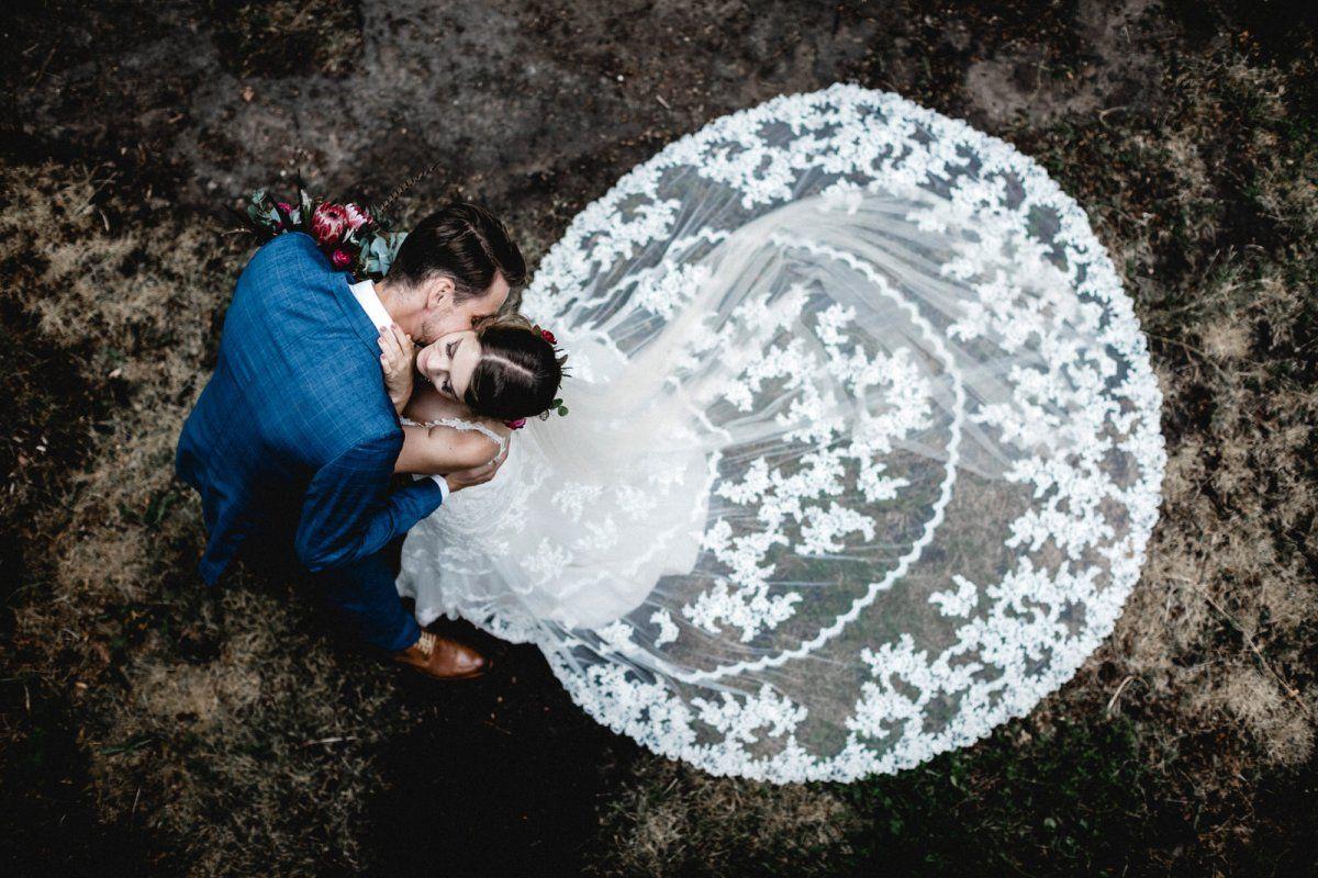 Eine Braut und ein Bräutigam küssen sich im Gras.