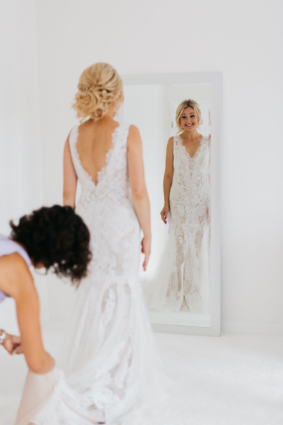 Die Braut trägt ein weißes Hochzeitskleid und betrachtet sich glücklich im Spiegel.