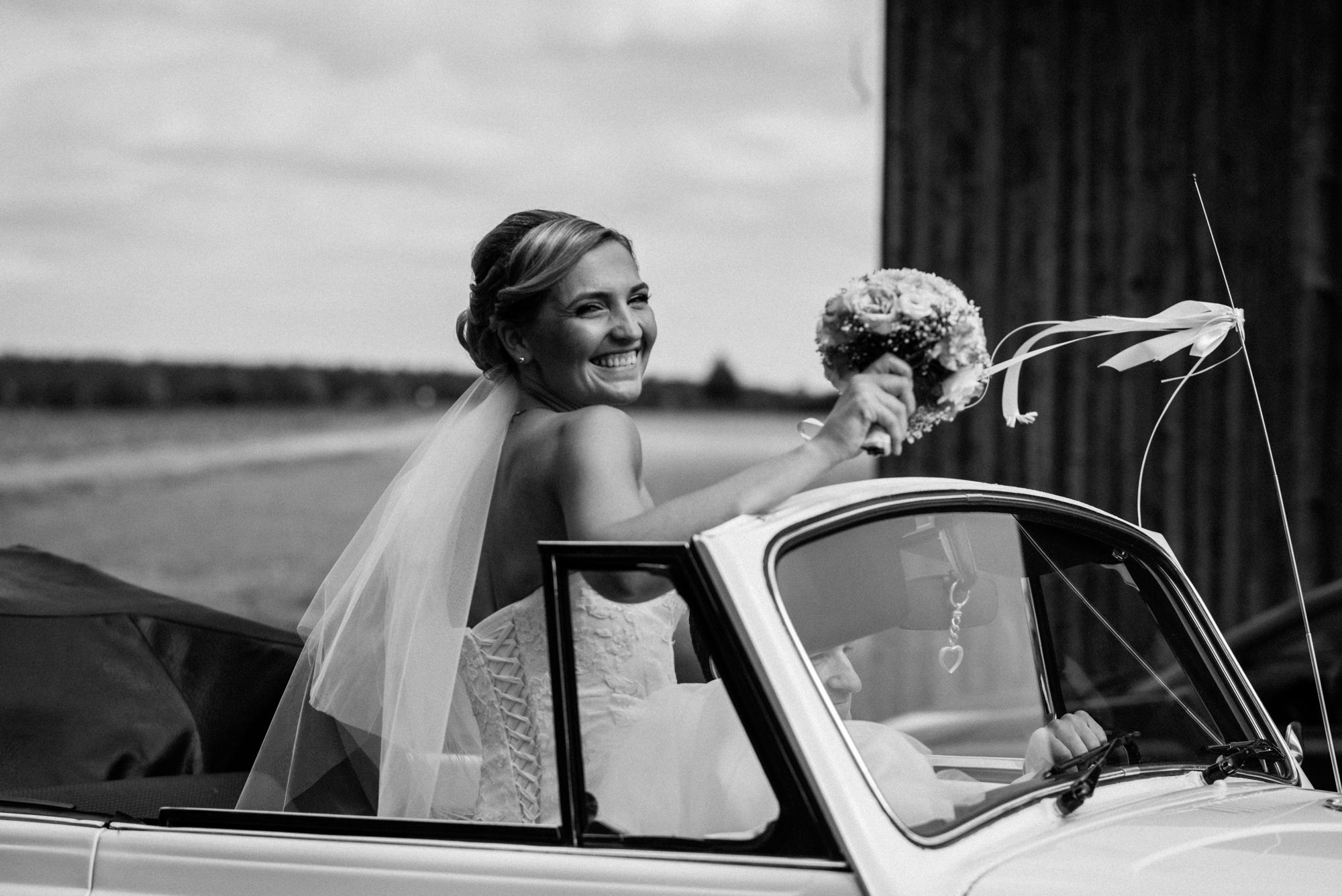 Schwarz-weiß-Aufnahme einer Braut, die lachend im Auto sitzt.
