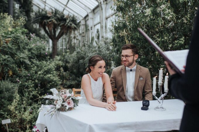 Eine Braut und ein Bräutigam sitzen an einem Tisch in einem Gewächshaus.