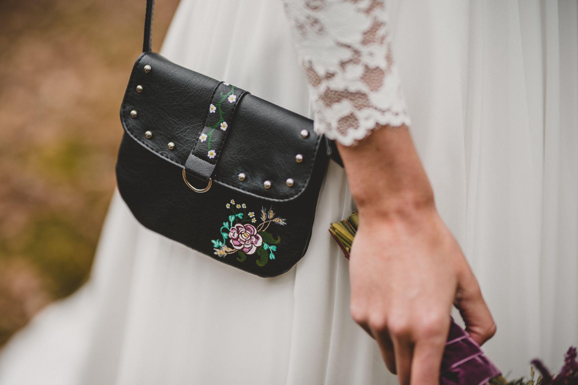 Eine Braut hält eine schwarze Handtasche mit Blumen darauf.