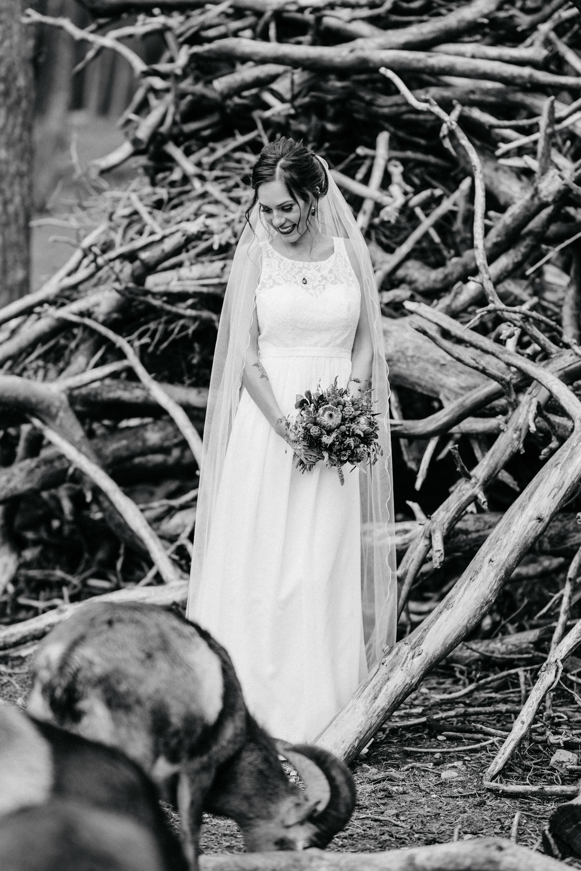 Schwarz-weiß-Aufnahme einer Braut, die in ihrem weißen Kleid in der Natur steht.