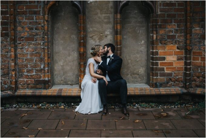Ein Brautpaar küsst sich vor einem alten Gebäude.