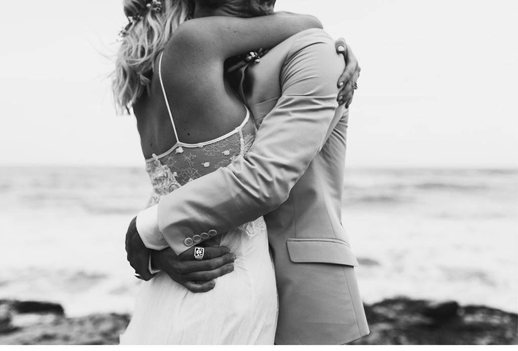 Eine Braut und ein Bräutigam umarmen sich am Strand.