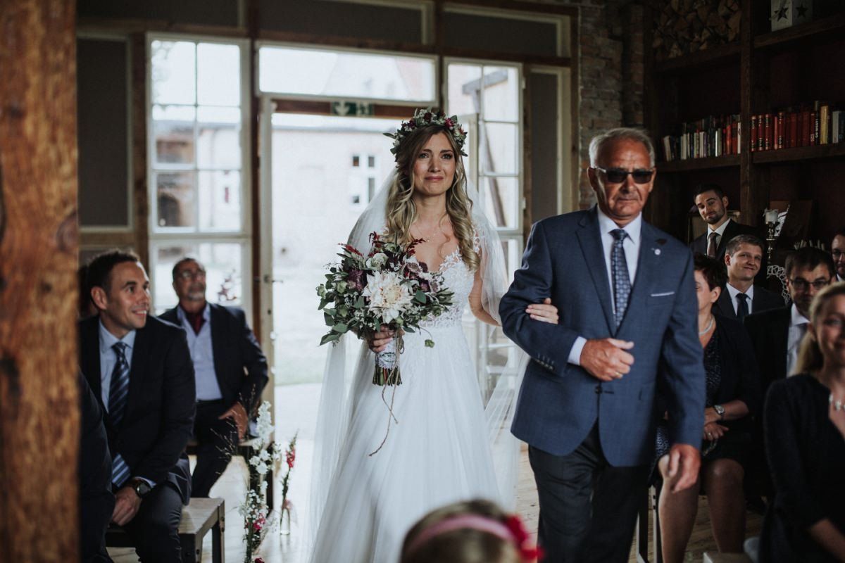 Eine Braut geht mit ihrem Vater den Gang entlang.