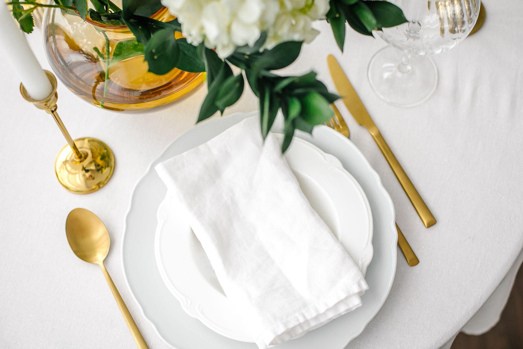 Ein weißer Tisch mit goldenen Utensilien und Servietten.