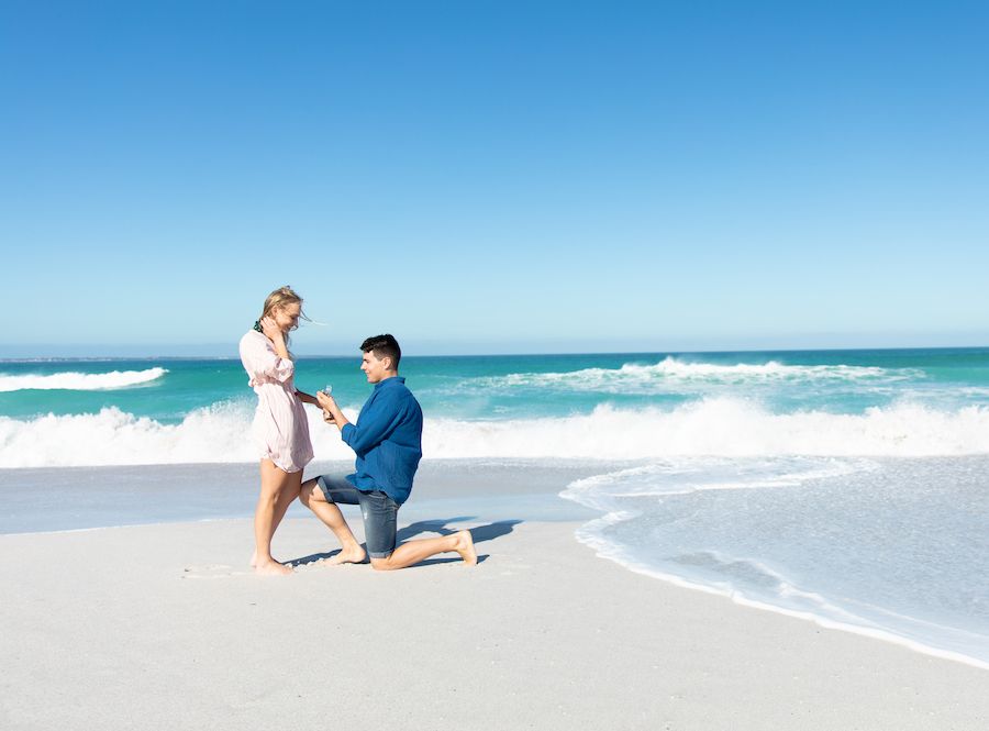 Ein Paar kniet am Strand und macht einander einen Heiratsantrag.