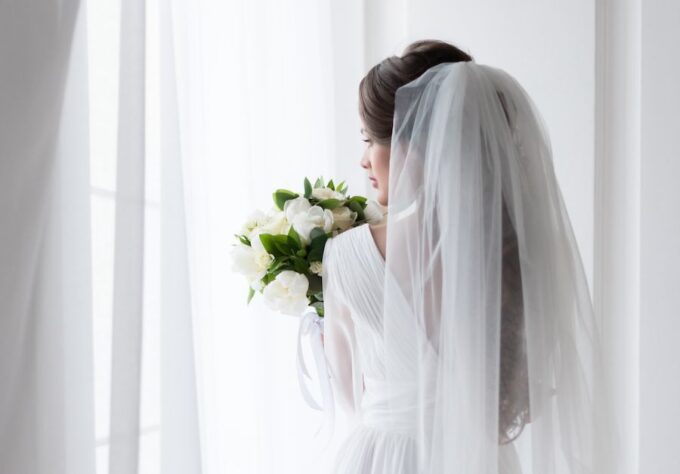 Eine Braut in einem weißen Hochzeitskleid schaut aus einem Fenster.