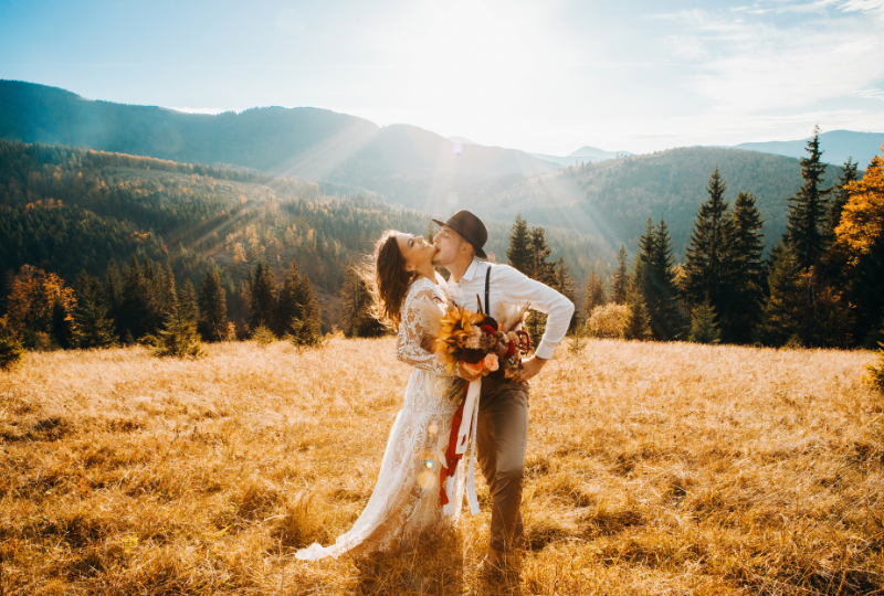 Eine Braut und ein Bräutigam küssen sich auf einem Feld mit Bergen im Hintergrund.