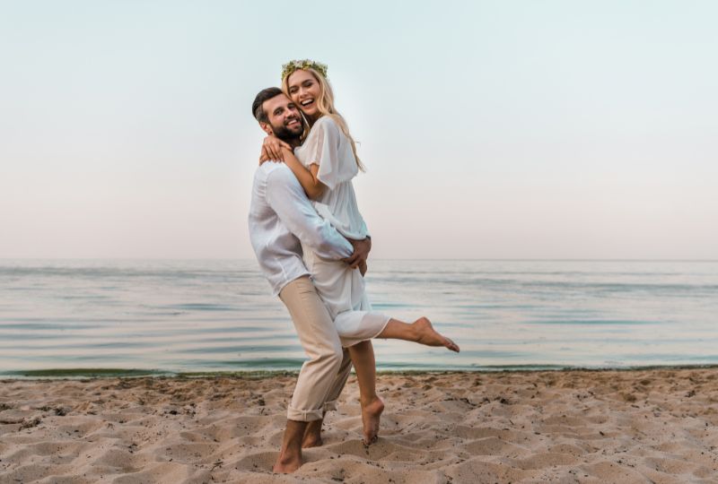 Das Brautpaar ist am Strand und lächelt glücklich.