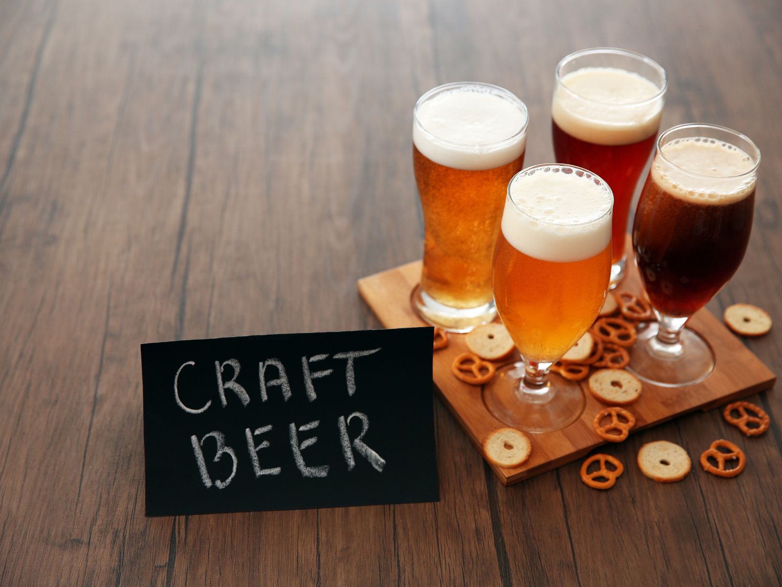 Vier Gläser Craft-Bier und Brezeln auf einem Holztisch.