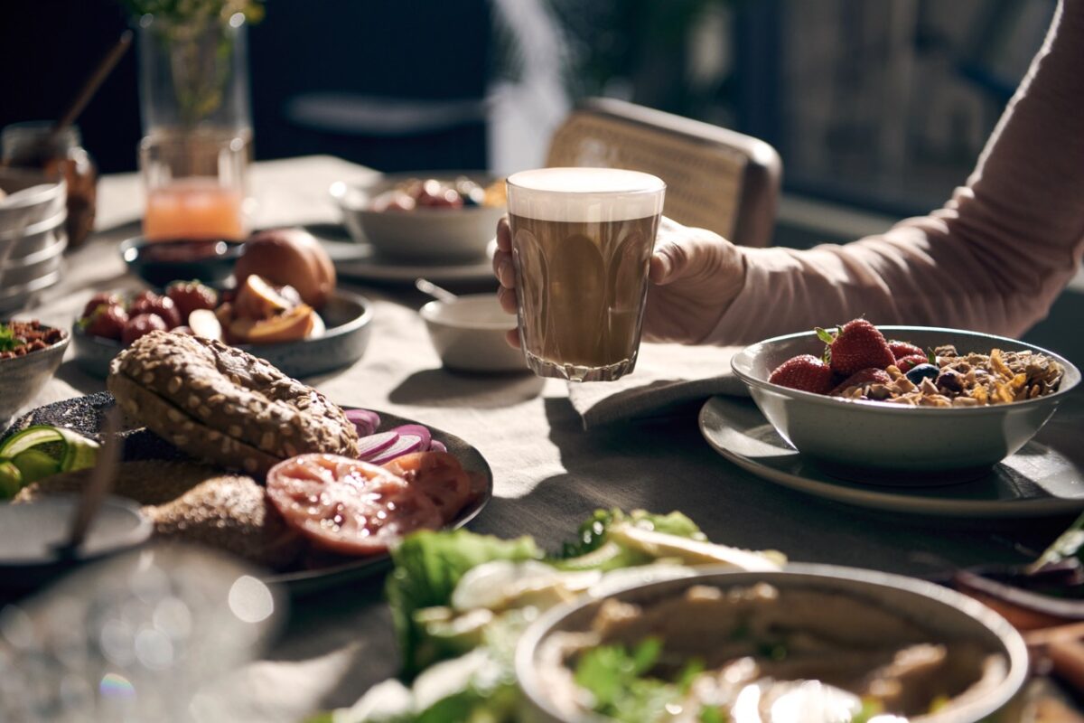 Eine Person hält eine Tasse Kaffee an einem Tisch voller Essen.