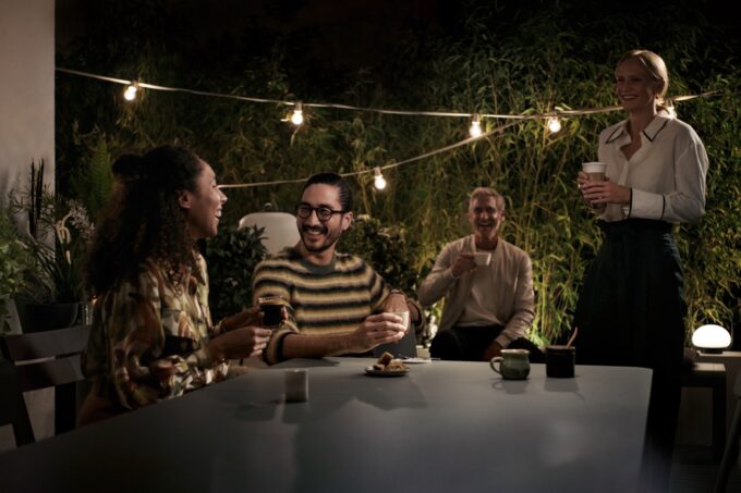 Vier Freunde genießen einen Abend bei einem Treffen im Freien unter Lichterketten.