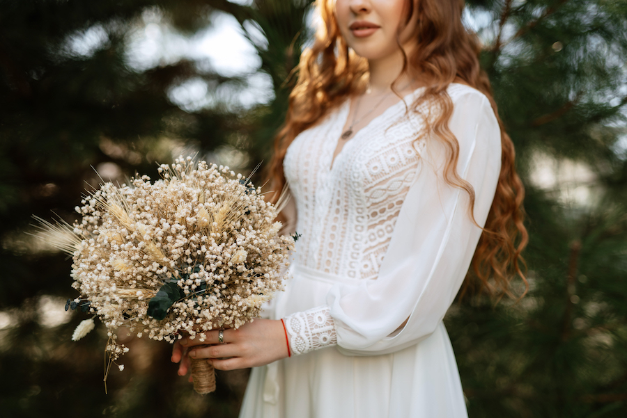 Eine schöne Frau in einem weißen Kleid hält einen Strauß getrockneter Blumen.