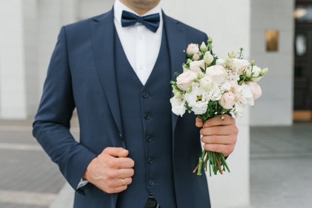 Bräutigam im Hochzeitsanzug hält den Brautstrauß in der Hand