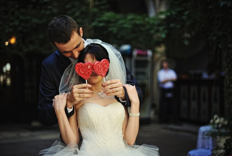 Eine Braut und ein Bräutigam mit roten herzförmigen Lutschern.