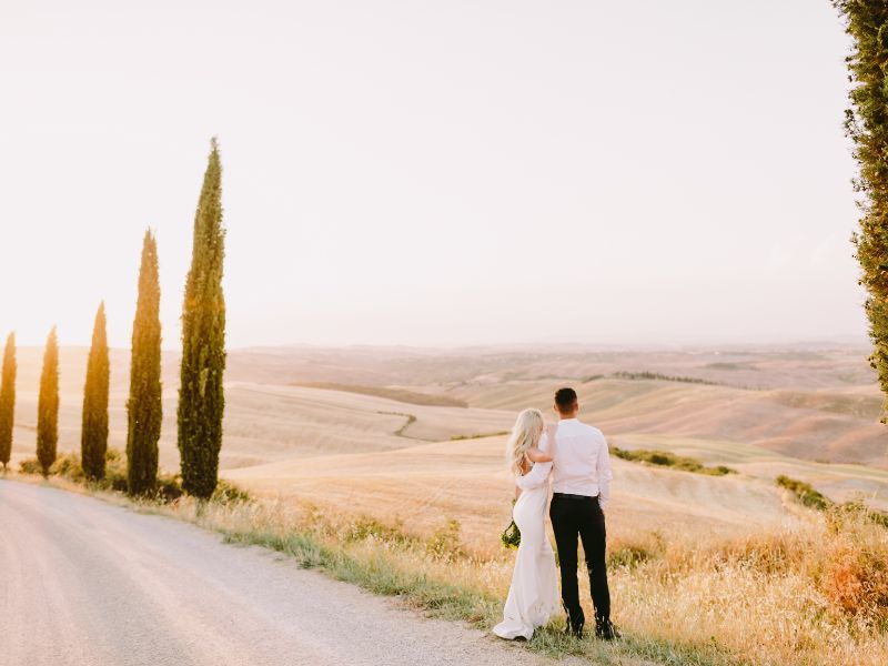 Brautpaar steht am Wegesrand in der Toskana mit Blick über die Felder
