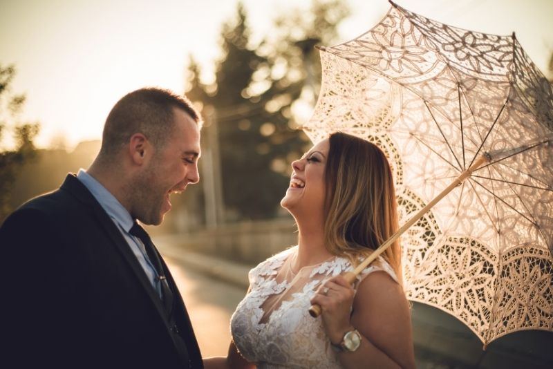 Das Brautpaar posiert mit einem Sonnenschirm.