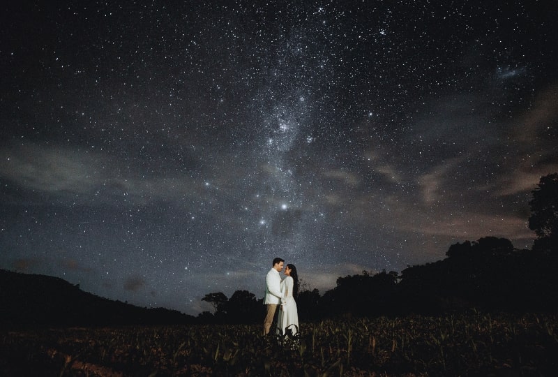 Eine Braut und ein Bräutigam stehen unter den Sternen auf einem Feld.