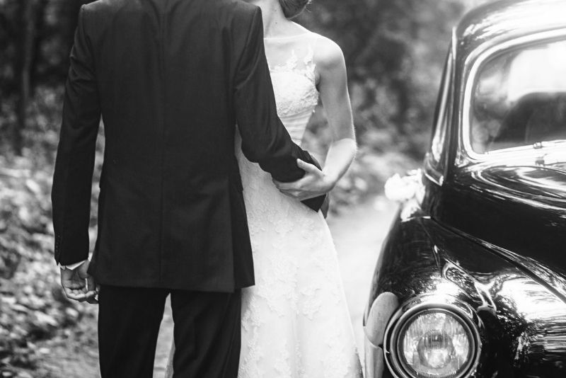 Das Brautpaar steht neben einem Auto.