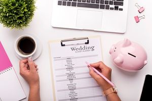 Eine Frau schreibt eine Hochzeitscheckliste auf einem Schreibtisch mit einem rosa Sparschwein.